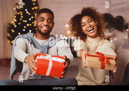 Merry Christmas! Joyful afro couple stretching xmas gifts Stock Photo