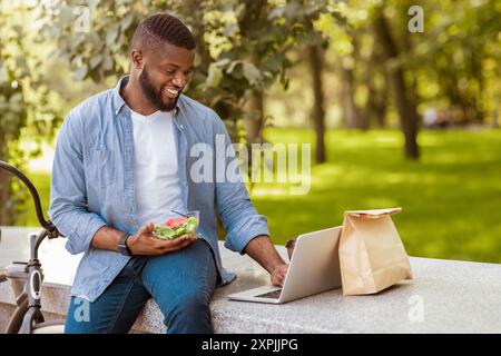 Happy afro businessman using laptop and having healthy lunch outdoors Stock Photo