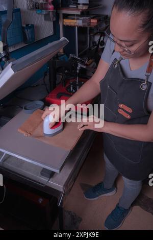 Young working woman in her workshop makes the sublimation process with a label plate, printing and graphic design concept. Stock Photo
