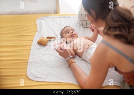 Mother and daughter playing hand-holding during diaper changing. Motherhood. Stock Photo