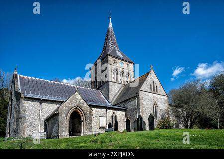 All Saints church in East Meon, Hampshire, against a bright blue sky, looking up from the roadside Stock Photo