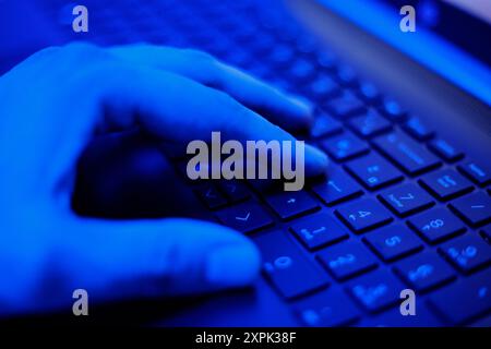 A hand hovers above the keys of a keyboard, illuminated by a soft blue glow that creates an ethereal atmosphere. The fingers are poised to type as the Stock Photo
