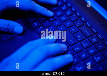 The focus highlights hands actively typing on a laptop keyboard, illuminated by a soft blue glow. The serene atmosphere suggests late-night productivi Stock Photo