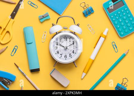 Top view of composition with school supplies and white alarm clock with space for text over yellow background. Back to school concept Stock Photo