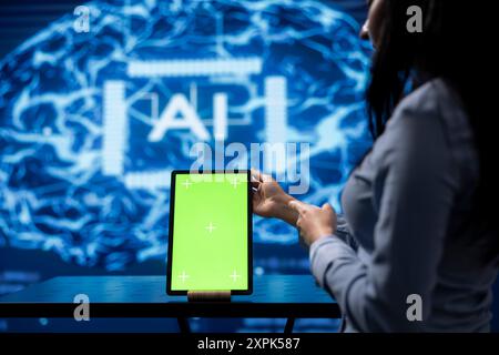 Startup coworkers brainstorming ways to use AI on chroma key tablet to improve data driven decisions. Technicians using mockup device to improve artificial intelligence tech Stock Photo