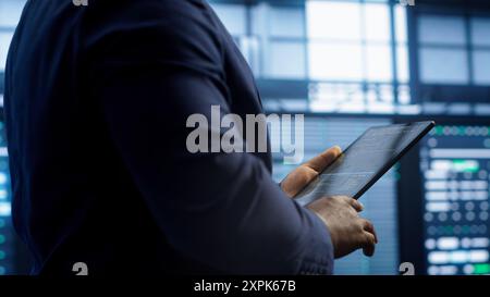 Technician walking in server room, doing checkup, inputting data on tablet of needed fixes. IT professional working in data center facility housing storage infrastructure, camera A Stock Photo