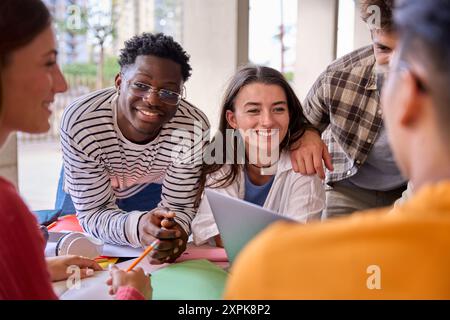 Cheerful multiracial couple of young students working together with classmates sitting in faculty. Stock Photo