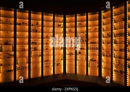 Smithsonian National Postal Museum Newspaper Exhibit Washington DC | WASHINGTON D.C., United States — A wide-angle view of the illuminated newspaper-rack exhibit at the Smithsonian National Postal Museum shows dozens of historic front pages glowing along an angular corridor. The installation underscores how closely American journalism and mail distribution were once linked, long before digital news made postal delivery unnecessary for daily papers. Stock Photo