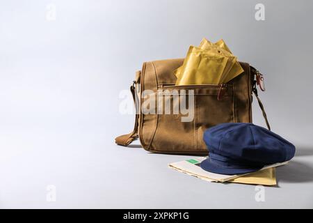 Brown postman's bag, envelopes, newspapers and hat on grey background. Space for text Stock Photo