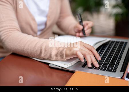 A cropped image of a woman in a cardigan typing on a laptop keyboard or pressing the Enter button to pause a video while studying an online class on h Stock Photo