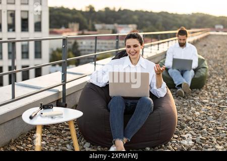 Colleagues working outdoors on rooftop with laptops Stock Photo