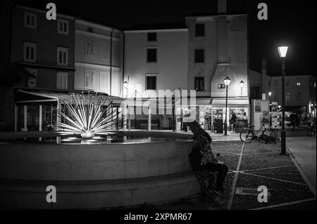 Cres, Croatia - October 23, 2022: Fountain near harbor in the night, people, black and white Stock Photo