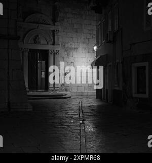 Cres, Croatia - October 23, 2022: Narrow street in Cres with old streetlamps during night, black and white Stock Photo