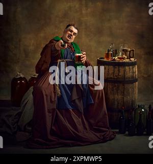 Sport fan supporting soccer team. Emotional monk in period attire watching game, drinking beer gain dimly lit vintage background. Stock Photo