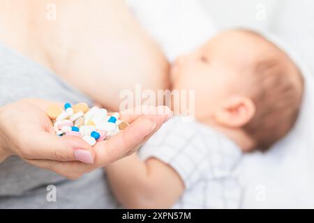 Mother holding handful of pills and tablets while breastfeeding newborn baby. Breastfeeding and medication concept Stock Photo