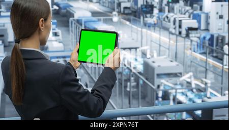 Electronics Manufacturing Project Manager Working on a Tablet Computer with Green Screen Template at a Factory. Female Specialist Developing, Maintaining, Upgrading Programs for Machine Production Stock Photo