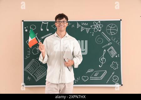 Male Italian teacher with flag and laptop near blackboard in classroom Stock Photo