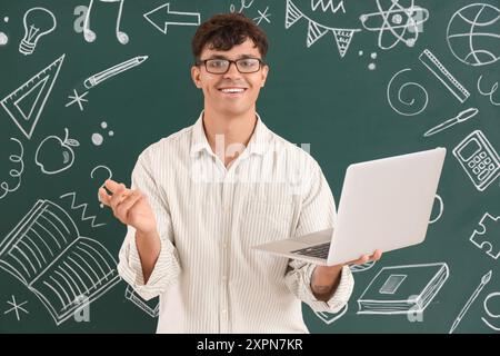Male teacher with laptop near blackboard in classroom Stock Photo