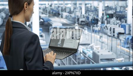 Electronics Manufacturing Technician Working on a Laptop Computer at a Factory Space. Female Specialist Developing, Maintaining, Upgrading Programs for Machine Production and Assembly Stock Photo