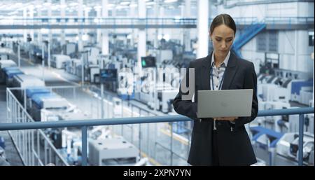 Electronics Manufacturing Technician Working on a Laptop Computer at a Factory Space. Female Specialist Developing, Maintaining, Upgrading Programs for Machine Production and Assembly Stock Photo