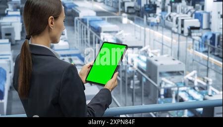 Electronics Manufacturing Project Manager Working on a Tablet Computer with Green Screen Template at a Factory. Female Specialist Developing, Maintaining, Upgrading Programs for Machine Production Stock Photo