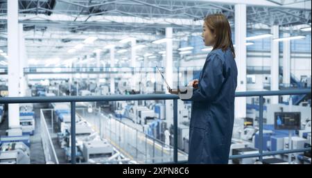 Electronics Manufacturing Technician Working on a Laptop Computer at a Factory Space. Asian Female Specialist Developing, Maintaining, Fine-Tuning Programs for Machine Production and Assembly Stock Photo