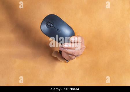 Close up of female hand holding a wireless mouse comes out tearing the brown paper. Stock Photo
