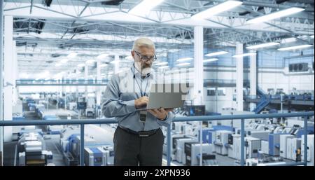 Thoughtful Middle Aged Engineer Monitoring and Analyzing Conditions at a Pristine Modern Electronics Factory with Automated Mobility Robots Working with the Help of Artificial Intelligence Software Stock Photo