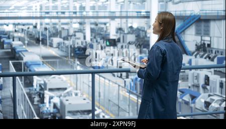 Japanese Factory Manager Working on a Tablet at a Futuristic Industrial Manufacture with Autonomous AI Robots. Specialist Monitoring All the Data on a Device, Checking Reports and Planning Research Stock Photo