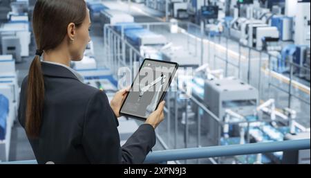Portrait of a Beautiful Happy Engineer Using Laptop Computer and Looking Around a Factory Facility with Automated Robotic Arms Producing Modern Electronic Components for Different Industries Stock Photo