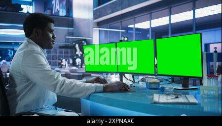 Cancer Research Center Medical Laboratory: Black Male Neuroscientist Using Desktop Computer With Green Screen Chromakey On Display. Specialist Studying Brain Tumor, Finding Solutions, Treatment. Stock Photo