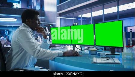 Cancer Research Center Medical Laboratory: Black Male Neuroscientist Using Desktop Computer With Green Screen Chromakey On Display. Specialist Studying Brain Tumor, Finding Solutions, Treatment. Stock Photo