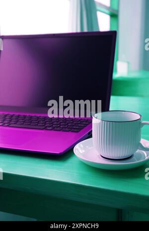 Pop Art of Ultramarine Purple Opened Laptop with a Coffee Cup on Mint Green Table Stock Photo