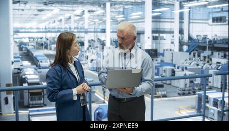Industrial Engineers Working at a Technology Factory. Caucasian Man and Japanese Female Using Laptop Computer and Having a Conversation. Portrait of a Couple at Work Stock Photo