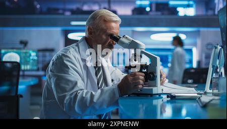 Medical Development Laboratory: Senior Caucasian Male Scientist Using Microscope, Analyzes Petri Dish Sample. Big Pharmaceutical Lab Conducting Biotechnology Research, Developing Innovative Drugs. Stock Photo