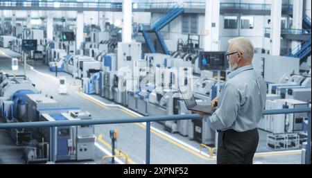 Electronics Manufacturing Technician Working on a Laptop Computer at a Factory Space. Specialist Developing, Maintaining, Fine-Tuning Programs for Machine Production and Assembly Stock Photo