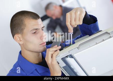 young serviceman in overall working on fridge Stock Photo