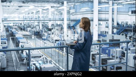 Japanese Factory Manager Working on Laptop at a Futuristic Industrial Manufacture with Autonomous AI Robots. Specialist Monitoring All the Data on a Computer, Checking Reports and Planning Research Stock Photo