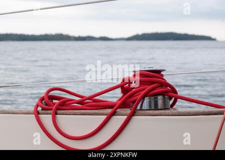 Sailboat winch with red rope of genoa headsail sheet on yacht deck. Detail, low depth of focus. Stock Photo