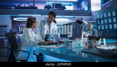 Asian And Caucasian Female Doctors Talking In Medical Research Center And Using Desktop Computer To Analyze Brain CT Scans. Surgeon And Neuroscientist Discussing Solutions For Treating Cancer Patients Stock Photo