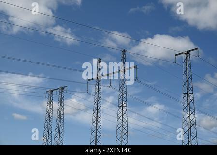 Transmission line pylon towers with cross arms, overhead lines, wires, conductors, spacers, dampers, insulators, earth wire.  Pylons against blue sky. Stock Photo