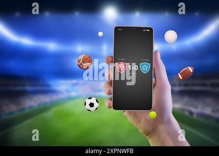 Mobile phone in hand displaying match results on an app, with various sports balls flying around it. Online live scores and sports betting Stock Photo