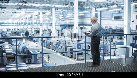 Thoughtful Middle Aged Engineer Monitoring and Analyzing Conditions at a Pristine Modern Electronics Factory with Automated Mobility Robots Working with the Help of Artificial Intelligence Software Stock Photo