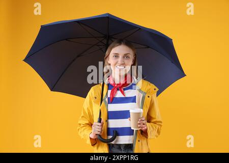 Woman with blue umbrella and paper cup on yellow background Stock Photo
