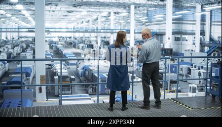 Middle Aged Engineer and Young Japanese Technician Having a Conversation and Using Laptop Computer. Specialists Monitoring, Analyzing Software Reports at a Modern Electronics Factory Stock Photo