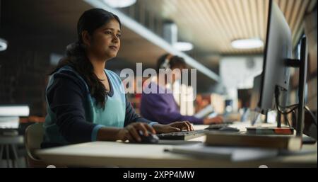Thoughtful Indian Female Student Working on Personal Development in a Quiet Public Library with Rows of Bookshelves. Young Smart South Asian Woman Preparing for Examination in College Stock Photo
