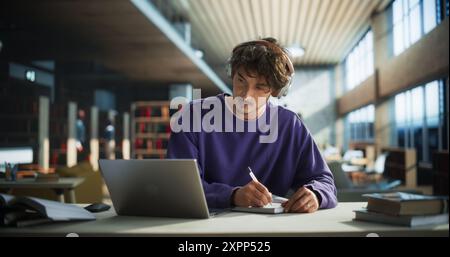 Thoughtful Young Student Preparing for Class, Doing Homework on a Laptop Computer. Freelance Journalist Working on an Article in a Public Library with Modern Simple Interior Stock Photo