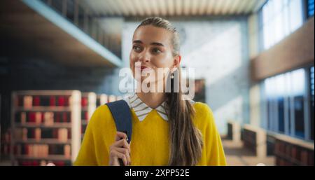 Close Up Portrait of a Happy Smiling Young Student Walking Indoors in University Campus. Joyful Female Wearing a Yellow Jumper, Looking Around the Library, Searching for Textbooks for Lecture Stock Photo