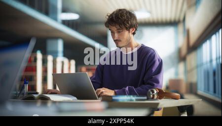 Portrait of a Stylish Male Student Working on His University Exercise on a Laptop Computer. Young Handsome Man Studying an Online College Course in an Empty Quiet Public Library Stock Photo