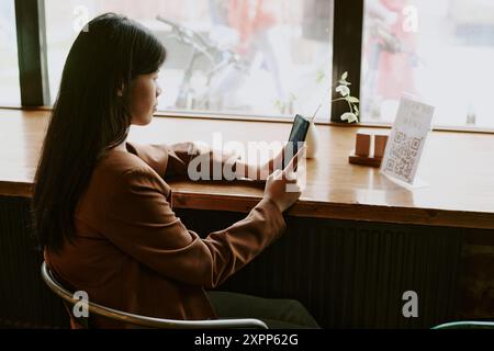 Asian Woman Sitting by Window Using Smartphone Stock Photo